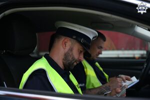 Zdjęcie przedstawia dwóch policjantów ruchu drogowego, którzy znajdują się w radiowozie i wykonują dokumentację