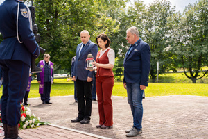 Na zdjęciu widoczni są trzej goście w trakcie składania znicza pod pomnikiem