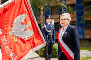 Na zdjęciu widoczny jest sztandar Policji, przed którym stoi zaproszony gość. W tle widoczny jest umundurowany policjant.