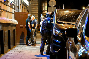 Na zdjęciu widoczny jest chodnik, na którym znajdują się policjanci oraz zaparkowane przy nim samochody