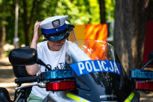 Na zdjęciu widoczny jest chłopiec, który siedzi na policyjnym motocyklu, a na głowie ma założoną czapkę policjanta