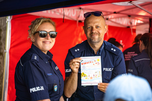 Na zdjęciu znajduje się dwóch policjantów, a jeden z nich trzyma w ręku plakat akcji - bezpieczne wakacje