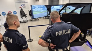 Zdjęcie przedstawia dwóch umundurowanych policjantów, w których tle widoczny jest symulator jazdy