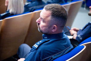 Zdjęcie przedstawia ze zbliżenia siedzącego policjanta.