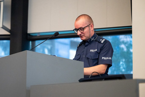 Zdjęcie przedstawia policjanta, który stoi za mównicą.