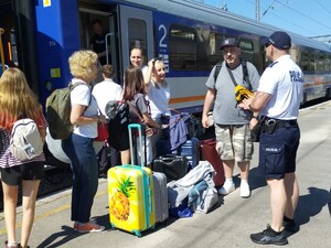 na zdjęciu widoczna jest do rodzina z dziećmi i bagażami na peronie wsiadająca do pociągu obok rodziny  nich stoi umundurowany policjant