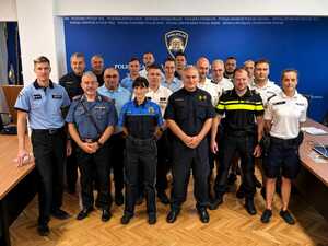 na zdjęciu widoczni stojący w szeregu w sali policjanci w różnych mundurach  po bokach kadru widoczne biurka w tle baner z napisem policja