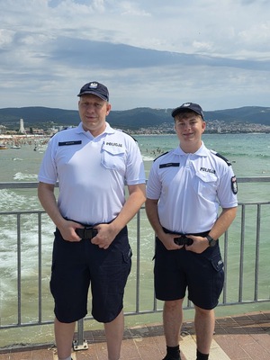 na zdjęciu widoczni są dwaj umundurowani policjanci stojący na molo, w tle widoczne morze i plaża