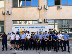 na zdjęciu widoczni są policjanci w różnych  mundurach  stojący w szeregu na tle pojazdu z napisem Policije 192 na dalszym planie fasada budynku