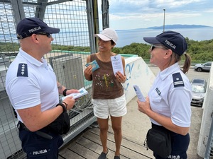 na zdjęciu widocznych jest dwóch umundurowanych policjantów rozmawiających z kobietą na drugim planie widoczna jest część drogi  i dalej drzewa i zatoka