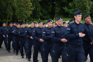 zdjęcie przedstawia maszerujących w kolumnie policjantów
