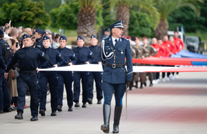 zdjęcie przedstawia policjantów niosących flagę i dowódcę uroczystości