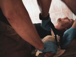 na zdjęciu w zbliżeniu widoczny leżący na plecach mężczyzna oraz widoczne dłonie w niebieskich rękawiczkach nitrylowych w trakcie zakładania opatrunku na lewe przedramię leżącego mężczyzny