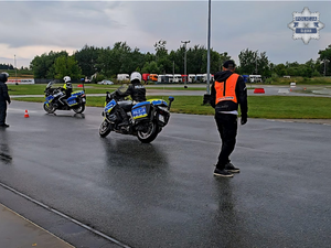 na zdjęciu widoczni na torze dwaj policjanci w czarnych kombinezonach motocyklowych i białych kaskach, poruszający się na oznakowanych motocyklach służbowych z napisem policja obok nich instruktor policyjny