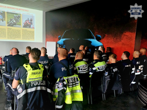 na zdjęciu widoczna salka wykładowa na której na krzesłach siedzi kilkunastu umundurowanych policjantów oglądających wyświetlane na ekranie slajdy dotyczące bezpiecznej jazdy motocyklem