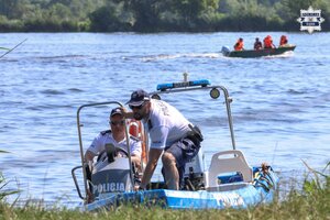 Dwaj policjanci na motorówce policyjneju płyną do brzegu. W oddali widoczni strażacy na motorówce.