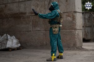 Osoba w kombinezonie ochronnym oraz masce gazowej na miejscu składowania odpadów..