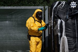 Osoba w kombinezonie ochronnym i masce gazowej na miejscu składowania odpadów.