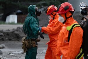 Osoba w kombinezonie i kasku ochronnym oraz maseczce na twarzy pomaga zdjąć kombinezon ochronny innej osobie, która ma maskę gazową.