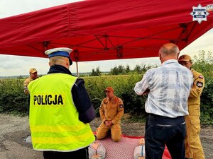 Na zdjęciu policjant, trzech strażaków i mężczyzna w koszuli pod czerwonym namiotem.