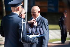 Na zdjęciu policjant oraz dwaj mężczyźni w momencie przypinania medalu