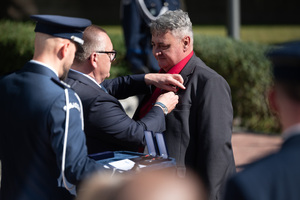 Na zdjęciu policjant oraz dwaj mężczyźni w momencie przypinania medalu