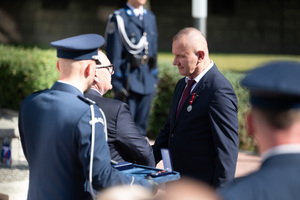 Na zdjęciu policjant oraz dwaj mężczyźni w momencie przypinania medalu