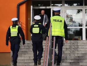 zbliżenie na trzech policjantów idących po schodach w stronę budynku szkoły