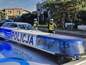 zbliżenie na dach policyjnego radiowozu, za którym stoją policjanci