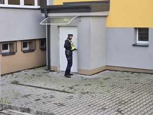 policjant trzyma dłoń na klamce drzwi z budynku szkoły