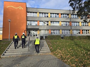 trzech policjantów idących po schodach w stronę budynku szkoły