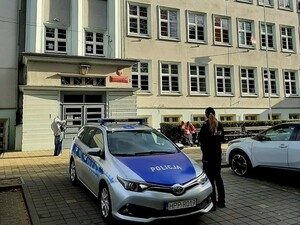 policjantka stojąca obok radiowozu przed budynkiem szkoły