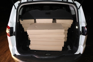 Kartony ułożone w bagażniku białego samochodu osobowego.