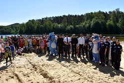 Grupa dzieci nad wodą wraz z przedstawicielami służb mundurowych oraz policyjnymi maskotkami