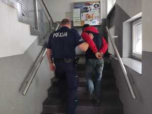 Policjant prowadzący zatrzymanego po schodach na terenie będzińskiej komendy.