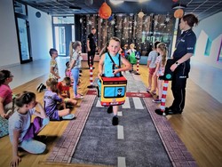 Na zdjęciu policjantka pokazuje dzieciom zastosowanie przepisów drogowych przy zastosowaniu mobilnego miasteczka.