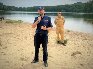 Na zdjęciu policjant przemawia na piasku podczas pikniku nad zalewem.