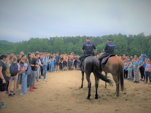 Na zdjęciu policjanci na koniach służbowych przemawiają do młodzieży.