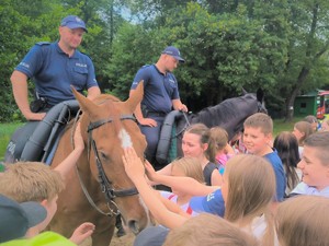 Na zdjęciu grupa dzieci podchodzi do policjantów na koniach.