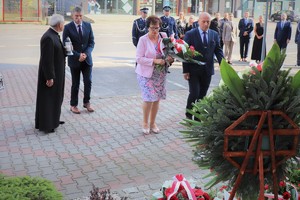 Na zdjęciu byli emerytowani policjanci w asyście kobiety oraz ksiądz podczas składania kwiatów i znicza pod tablica pamiątkową.