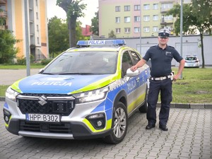 Na zdjęciu policjant stoi obok radiowozu.