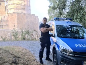 Na zdjęciu policjant stojący przy radiowozie.