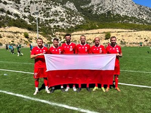 Na zdjęciu 6 mężczyzn w strojach piłkarskich, którzy trzymają flagę.