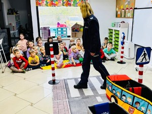 Na zdjęciu policjantka pokazuje grupie przedszkolaków jak przechodzić przez przejście dla pieszych.