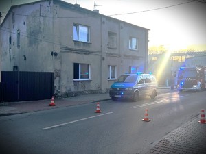 Na zdjęciu radiowóz policyjny i wóz strażacki zaparkowany przy budynku.