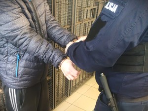 Na zdjęciu policjant zakłada kajdanki zatrzymanemu.