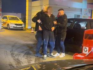 Na zdjęciu dwóch mężczyzn trzyma jednego obok jego samochodu.