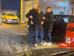 Na zdjęciu dwóch mężczyzn trzyma jednego obok jego samochodu.