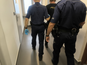 na zdjęciu policjanci prowadzą zatrzymanego mężczyznę