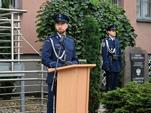 Na zdjęciu lektor uroczystości za mównicą przed budynkiem komendy.